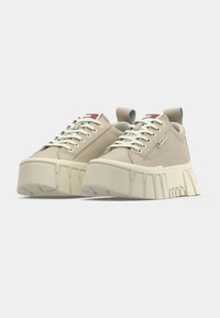 Sneaker beige con suola piatta chunky di colore crema. Parte superiore in sintetico liscio, lacci piatti e linguetta posteriore. Etichetta del marchio sul lato.