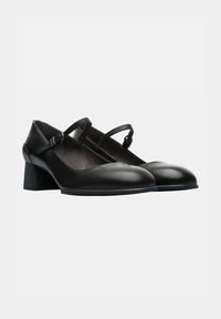 Black leather heels with a rounded toe and a low block heel. Features two adjustable straps across the foot. Smooth texture and minimalist design.
