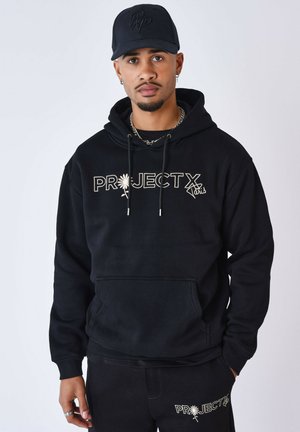 Haut à capuche noir avec le texte "PROJECT X" en crème, cordons de serrage et poche avant. Associé à un pantalon noir assorti.