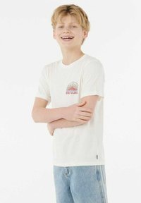 Camiseta blanca de manga corta con escote redondo y un diseño gráfico colorido con un estallido de sol. Combinada con unos vaqueros azul claro.