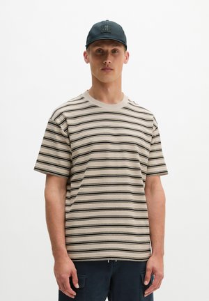 Mann trägt beige-schwarz gestreiftes kurzärmeliges Hemd, marineblaue Cargohose und schwarze Baseballkappe vor weißem Hintergrund.