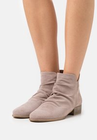 Bottines beiges en matériau perforé avec un design décontracté, bout pointu et un petit talon en bois empilé.