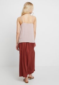 Ljusa rosa, ärmlös topp med tunna remmar, tillsammans med en lång, flödande kjol i rostfärg. Outfiten har en lös passform och en mjuk textur.