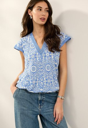 Top blu con motivo floreale, scollatura a V e maniche a cappuccio, con delicate rifiniture in pizzo blu chiaro. Abbinato a jeans in denim blu.
