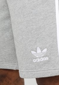 Gray Adidas shorts with white logo and white stripes worn by a person with dark skin visible on the lower leg.