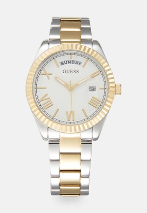 Relógio em metal prata e dourado com um mostrador branco, números romanos e um visor de data, apresentando uma luneta texturizada e uma pulseira de elos.