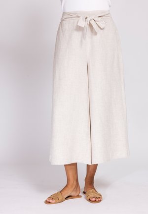 Beige wide-leg cropped pants with a tied belt at the waist, worn with tan slip-on flat sandals.