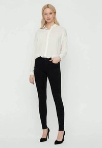 White button-up shirt with long sleeves, paired with black skinny jeans and black high heels. Smooth fabric and tailored fit.