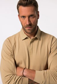 Beige Langarm-Polohemd mit klassischem Kragen, weicher Textur und einem dezenten Glanz. Es hat ein schlichtes Design ohne sichtbare Muster oder Logos.