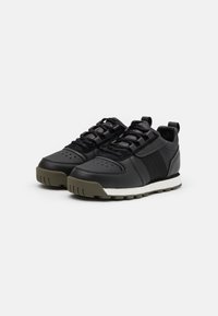 Black sneakers with a textured leather upper, lace-up design, padded tongue, rubber sole, and olive green accents. White midsole detail.