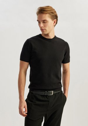 Sort kortærmet t-shirt med rund hals og tekstureret finish, båret med sorte bukser og et sort bælte med en sølvspænde.