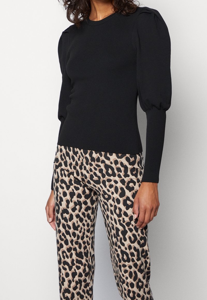 Top de punto negro con mangas abullonadas, combinado con pantalones beige que presentan un estampado de leopardo negro. Contrastes de textura considerables en el diseño.