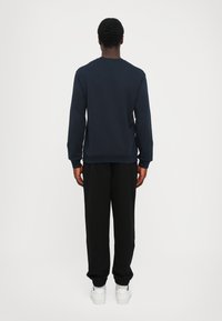 Navy blue sweatshirt with a crew neckline, ribbed cuffs, and a straight hem, paired with black tapered pants and white sneakers.