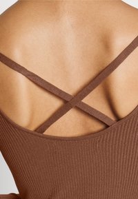 Brun ribbad klädesplagg med korsade remmar, som har en slät textur och en låg rygdesign som framhäver huden under.