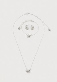 Σετ ασημένιων κοσμημάτων που περιλαμβάνει κολιέ, βραχιόλι και σκουλαρίκια. Διακοσμητικά σε σχήμα καρδιάς με περίτεχνη λεπτομέρεια και ένα μενταγιόν "Guess".