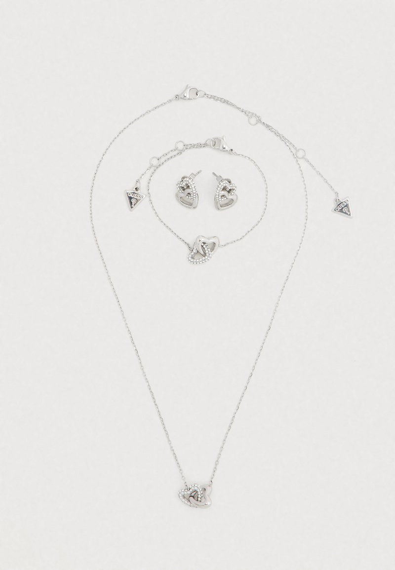 Ensemble de bijoux en argent comprenant un collier, un bracelet et des boucles d'oreilles. Ornements en forme de cœur avec des détails complexes et un pendentif "Guess".