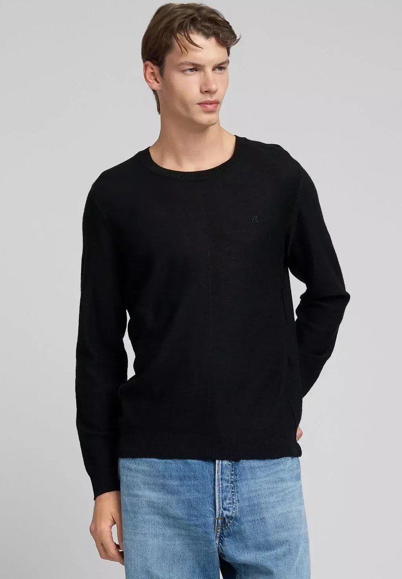 Suéter de punto negro con cuello redondo, mangas largas y puños acanalados. Textura sutil, combinado con vaqueros azul claro. Sin marcas visibles.