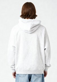 Felpa con cappuccio grigio chiaro con coulisse, polsini e orlo a coste, tessuto morbido e maniche raglan, indossata sopra jeans blu.