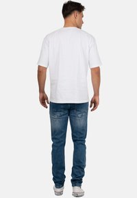 Witte T-shirt met korte mouwen en ronde hals, gecombineerd met lichtblauwe slim-fit jeans met een verouderde was en achterzakken. Witte sneakers maken de outfit compleet.