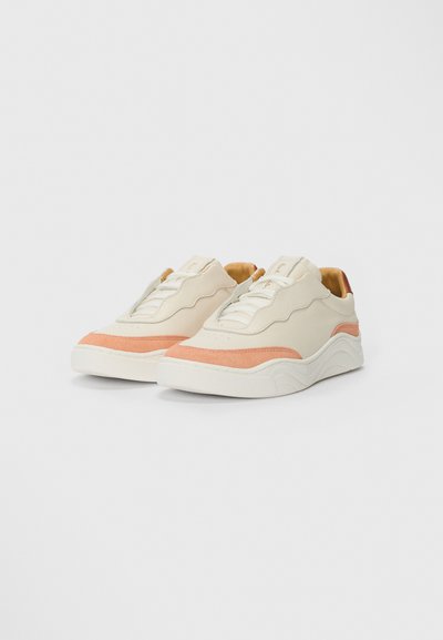 Sneaker di un beige chiaro con accenti corallo, caratterizzati da una tomaia testurizzata, punta arrotondata e un design della suola a strati. Lacci e logo visibili.