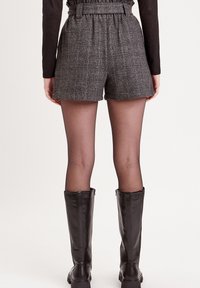 Shorts à carreaux gris avec une taille haute ceinturée, associés à des collants transparents et des bottes noires jusqu'aux genoux. Le tissu a une apparence texturée.