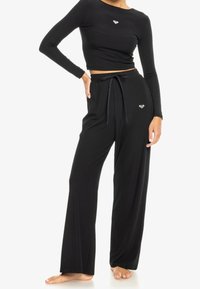 Černý žebrovaný dlouhý rukáv cropped top spárovaný s vysokými kalhotami širokého střihu s tkaničkou, obojí zdobené malým emblémem.