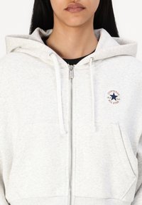 Light grey hooded sweatshirt in soft material, featuring a front zipper, white drawstrings, and a circular Converse logo on the chest.
