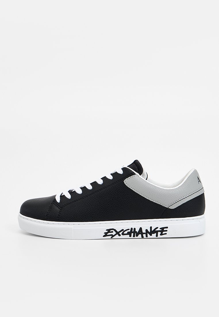 Sneaker nera con upper testurizzato, accenti grigi, suola bianca e branding decorativo sul lato. Presenta un sistema di allacciatura tradizionale.