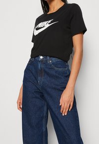 Camiseta de algodón negra con un gran logo blanco de Nike, combinada con unos vaqueros de mezclilla azul oscuro de talle alto, que muestran un ajuste relajado.