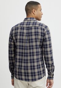 Cămașă pentru bărbați cu carouri în nuanțe de bleumarin și bej, având guler cu nasturi, mâneci lungi și tiv drept cu detalii discrete de cusătură.