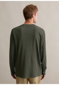 Langärmliges Hemd aus olivgrünem Baumwollstoff, lockere Passform, mit Rundhalsausschnitt und weicher Textur. Mit Bündchen und geradem Saum.