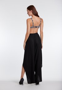 Black wide-leg pants with a high slit, paired with a patterned crop top featuring geometric black and white designs on thick straps.