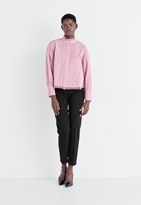 Pink long-sleeve shirt with collar and button detail, featuring scalloped accents and textured fabric, paired with black slim-fit trousers.