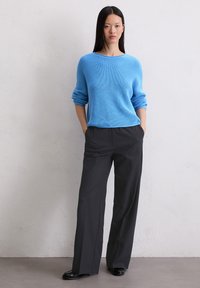 Pull en maille côtelée bleu clair à manches longues, associé à un pantalon large noir taille haute et des chaussures noires. Design simple et structuré.
