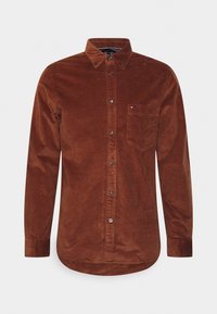 Hnědá kordurová košile s límcem na knoflíky, vybavená předními knoflíky a náprsní kapsou. Obsahuje jemnou texturu a zakřivený lem.