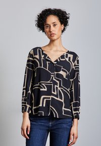 Blusa a maniche lunghe nera con motivi astratti beige, presenta una scollatura a V e dettagli con bottoni sul davanti. Tessuto morbido e leggero.