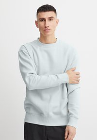 Lichtblauwe sweatshirt van zachte stof, met een ronde hals, ribgebreide manchetten en een klein label aan de onderlinkerkant.