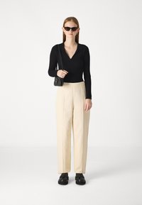 Polo a maniche lunghe ribbed nera, pantaloni beigi a vita alta con pieghe frontali, occhiali da sole neri rettangolari e borsa nera con tracolla.