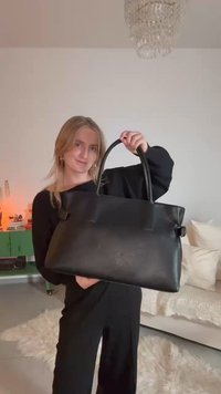 Black leather tote bag with dual handles, rectangular shape, textured surface, and minimalistic design, held against a neutral background.