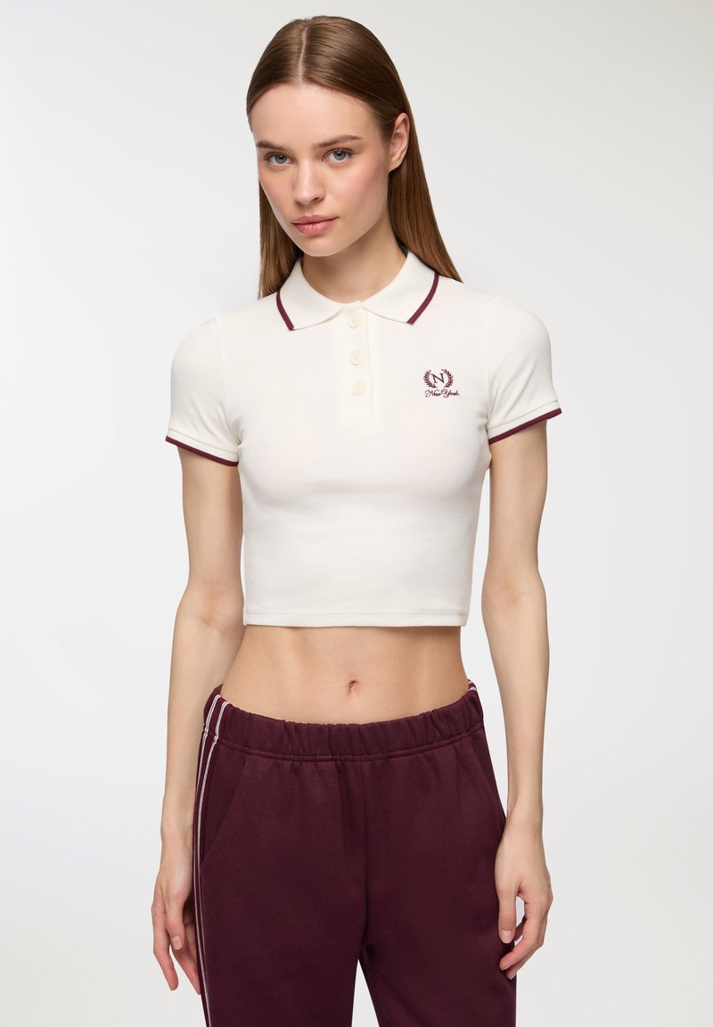 Polo shirt bianco corto con colletto e bordi bordeaux, dotato di tre bottoni e un piccolo logo ricamato sul lato sinistro del petto.