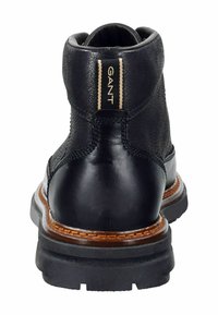 Černá kožená kotníková bota s texturovaným povrchem, výrazným podpatkem, hnědým prošíváním a značkovým štítkem na zadní straně.