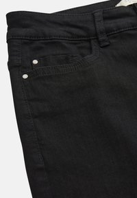 Schwarze Denim-Jeans Nahaufnahme, die die Vordertasche, den Gürtelriemen und Nieten-Details vor hellem Hintergrund zeigt.