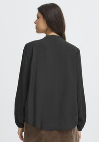 Long-sleeve black blouse with a textured finish. Features a round neckline and elastic cuffs, hem slightly longer in the back.