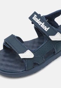 Sandalias azul marino con correas texturizadas y plantilla acolchada. Incluyen cierres ajustables de Velcro y un detalle del logo en blanco.