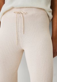 Beige strikkede leggings med et struktureret mønster, der har en snøre i taljen og en tætsiddende pasform, lavet af et blødt, strækbart materiale.