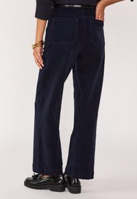Pantaloni in corduroy blu navy a gamba larga con tessuto testurizzato, due tasche posteriori e orlo leggermente accorciato, abbinati a scarpe oxford nere.