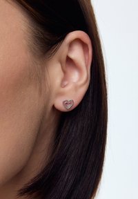 Srebrne kolczyki w kształcie serca z otwartym wzorem i wewnętrznym akcentem w formie czerwonego serca, z wypolerowaną powierzchnią.