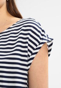 Granatowa i biała bluzka w paski z krótkimi, podwiniętymi rękawami, gładką teksturą i szerokim dekoltem. Posiada proste linie i minimalistyczny design.