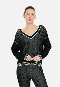 Maglione nero a maglia con scollo a V, con motivi argentati elaborati e accenti bianchi sui polsini e sull'orlo. Texture liscia, vestibilità comoda.