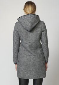 Cappotto in un pattern pied-de-poule bianco e nero con cappuccio, maniche lunghe e tasche laterali, caratterizzato da una silhouette aderente e un tessuto testurizzato.